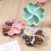 A hand is holding a light green heart-shaped four-compartment snack tray with various dried foods inside.