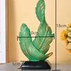 A vertical sculpture of a green feather with gold accents, mounted on a black base.