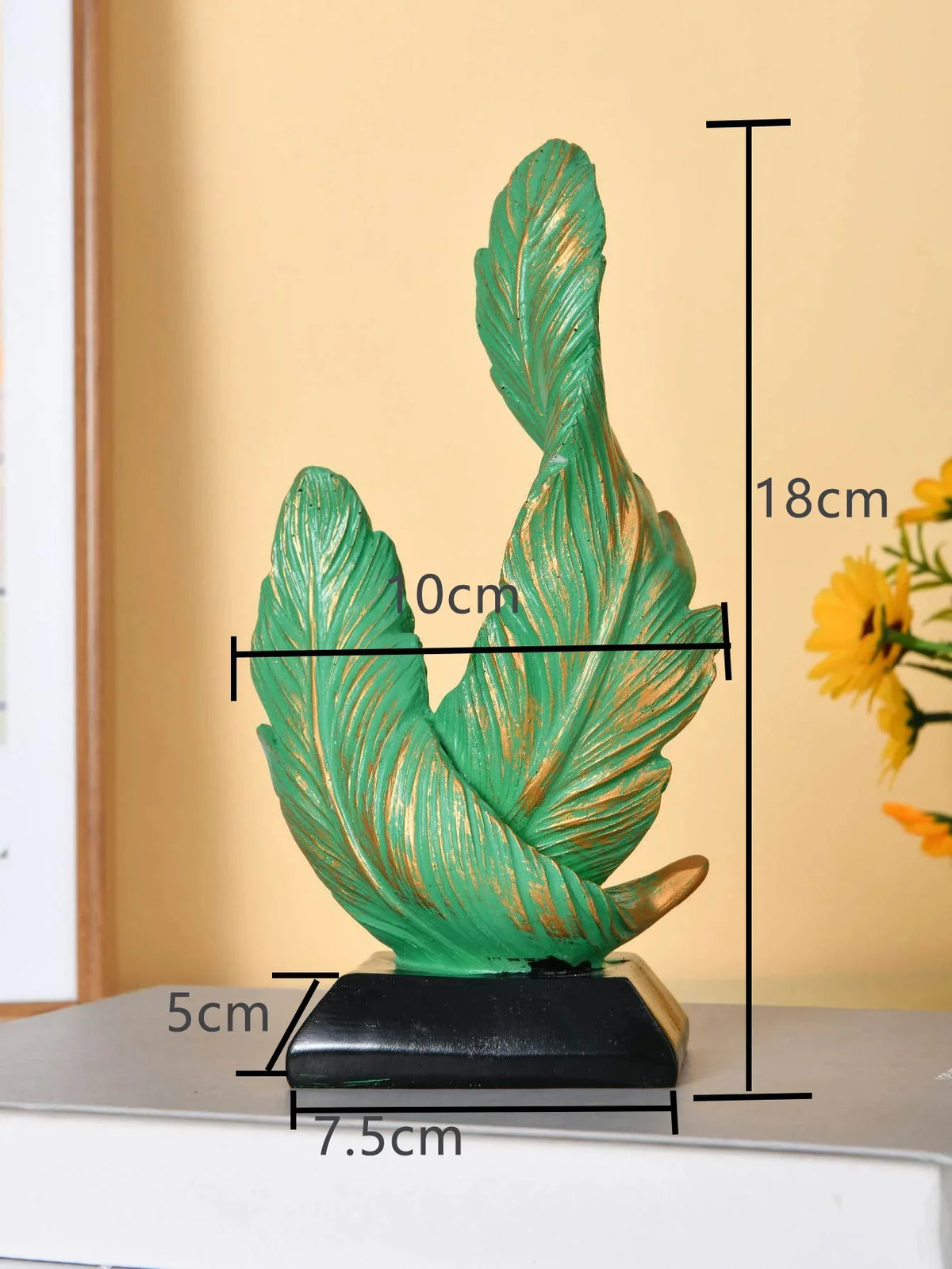 A vertical sculpture of a green feather with gold accents, mounted on a black base.