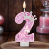 A pink glitter candle shaped like the number 2 with a crown and butterfly details
