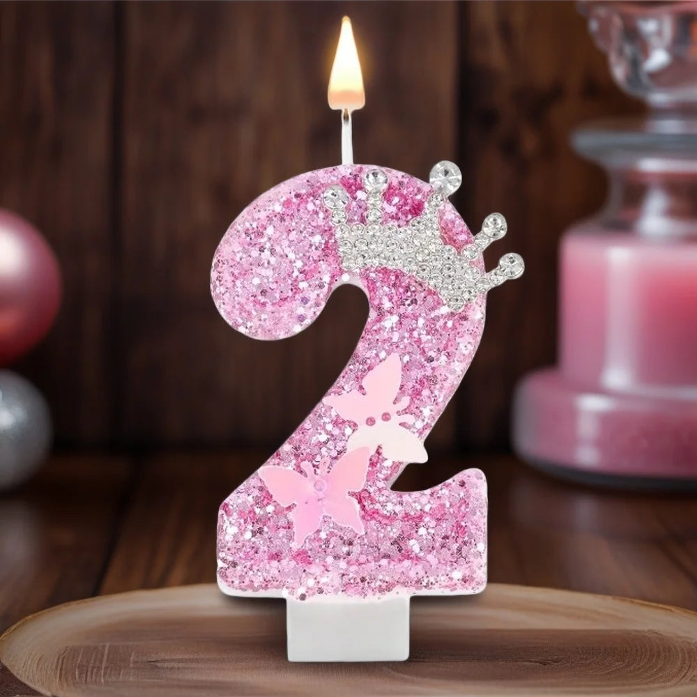 A pink glitter candle shaped like the number 2 with a crown and butterfly details