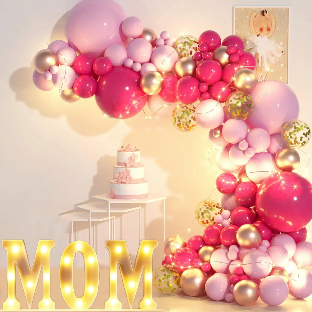 A pink and gold balloon garland arch display featuring balloons on a wall with a tiered cake.