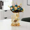 Gold ceramic swan vase filled with blue and peach flowers on a white table.