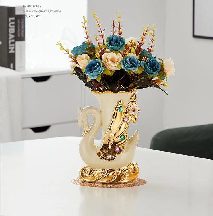 Gold ceramic swan vase filled with blue and peach flowers on a white table.