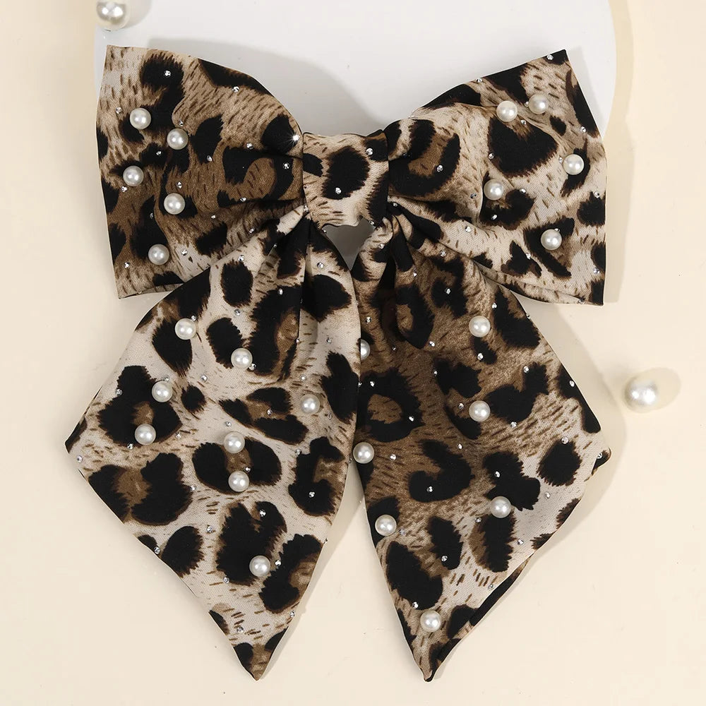 Une paire de pinces à cheveux en velours à imprimé léopard avec des taches noires et brunes et des embellissements de perles.