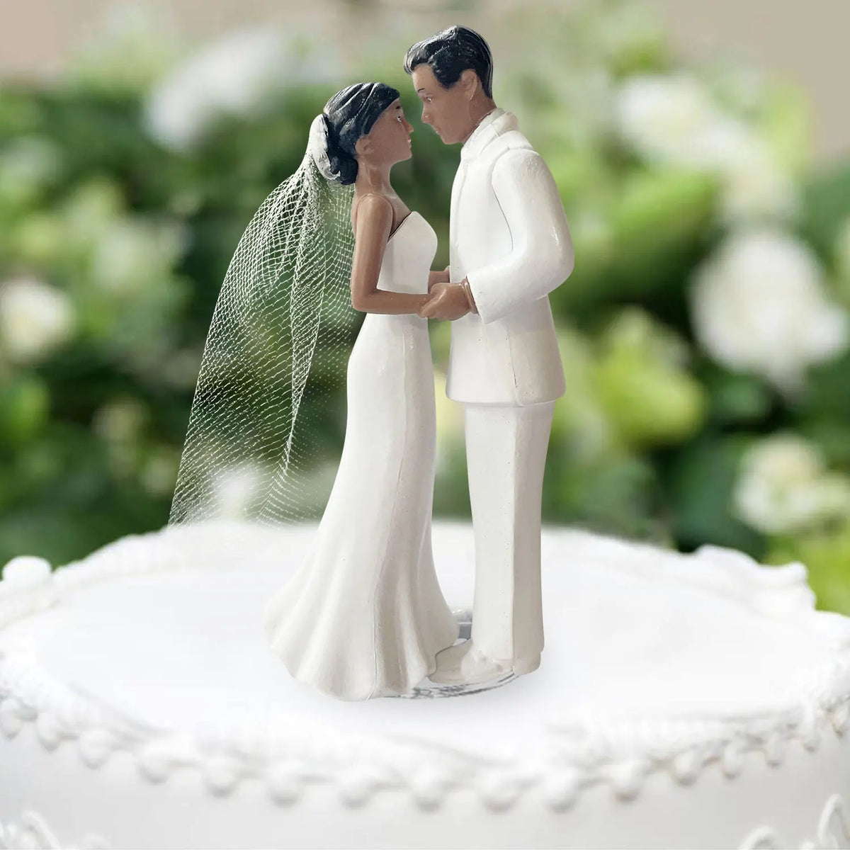 A wedding cake topper featuring a bride and groom figurine in white attire.