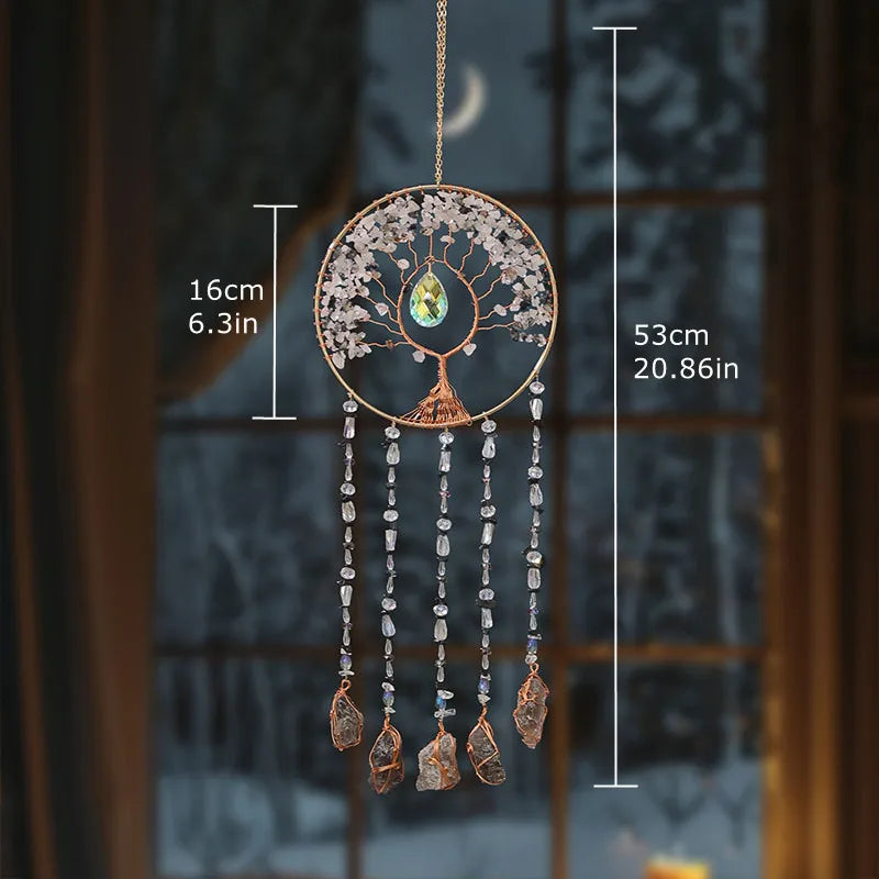 A hanging crystal tree of life sun catcher with branches and dangling crystals, displayed against a blurred window background