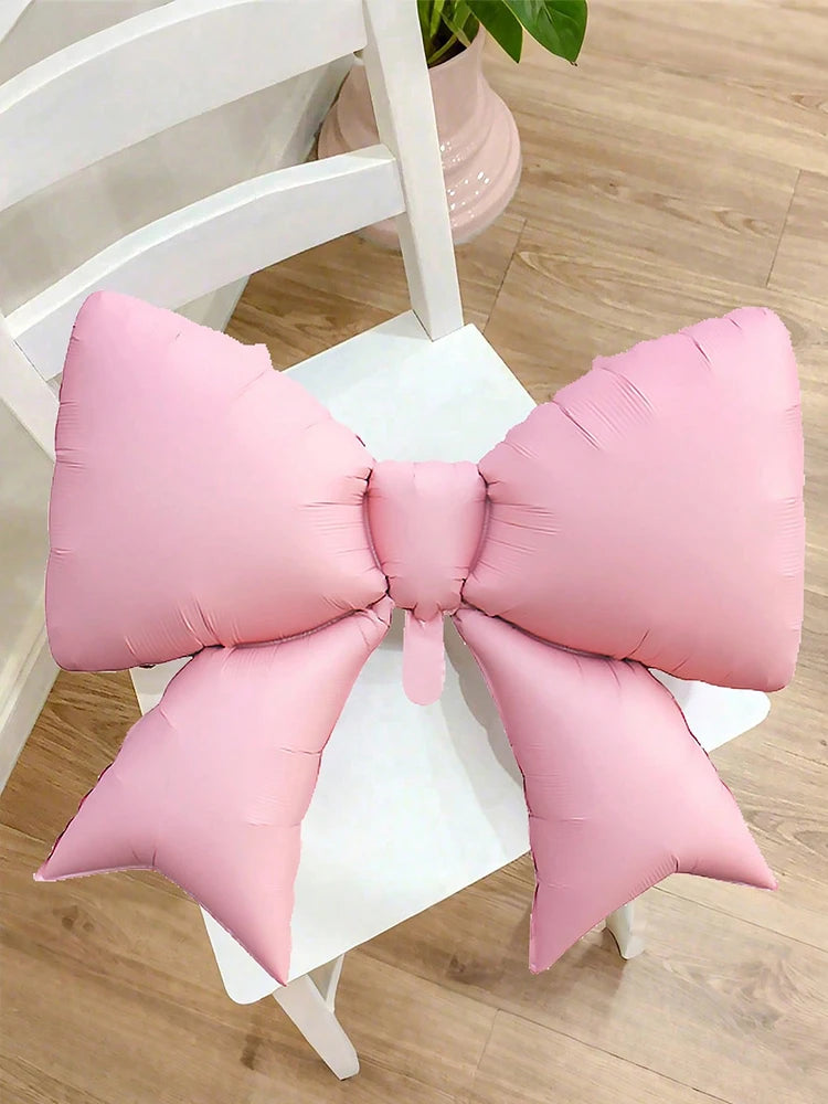 A pink balloon bow set used as a birthday banner decoration on a white table.