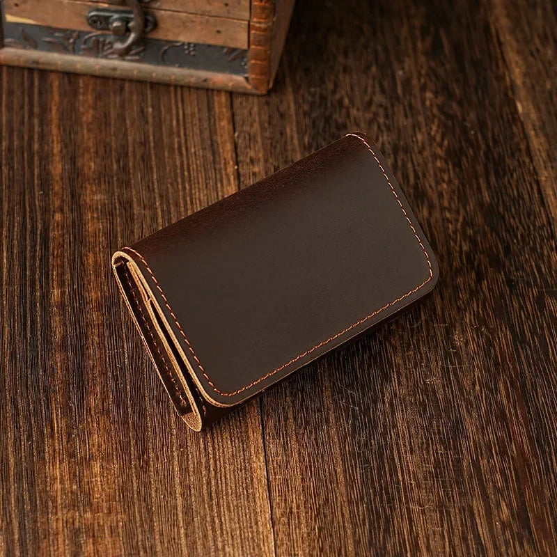 A dark brown leather card holder with stitched edges resting on a wooden surface.
