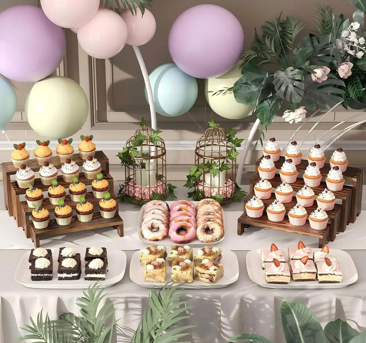 A display of various cupcakes and pastries arranged on wooden tiered stands with pastel balloons and greenery.