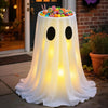 A white fabric ghost lantern with glowing yellow lights sits on a porch, filled with colorful Halloween treats.