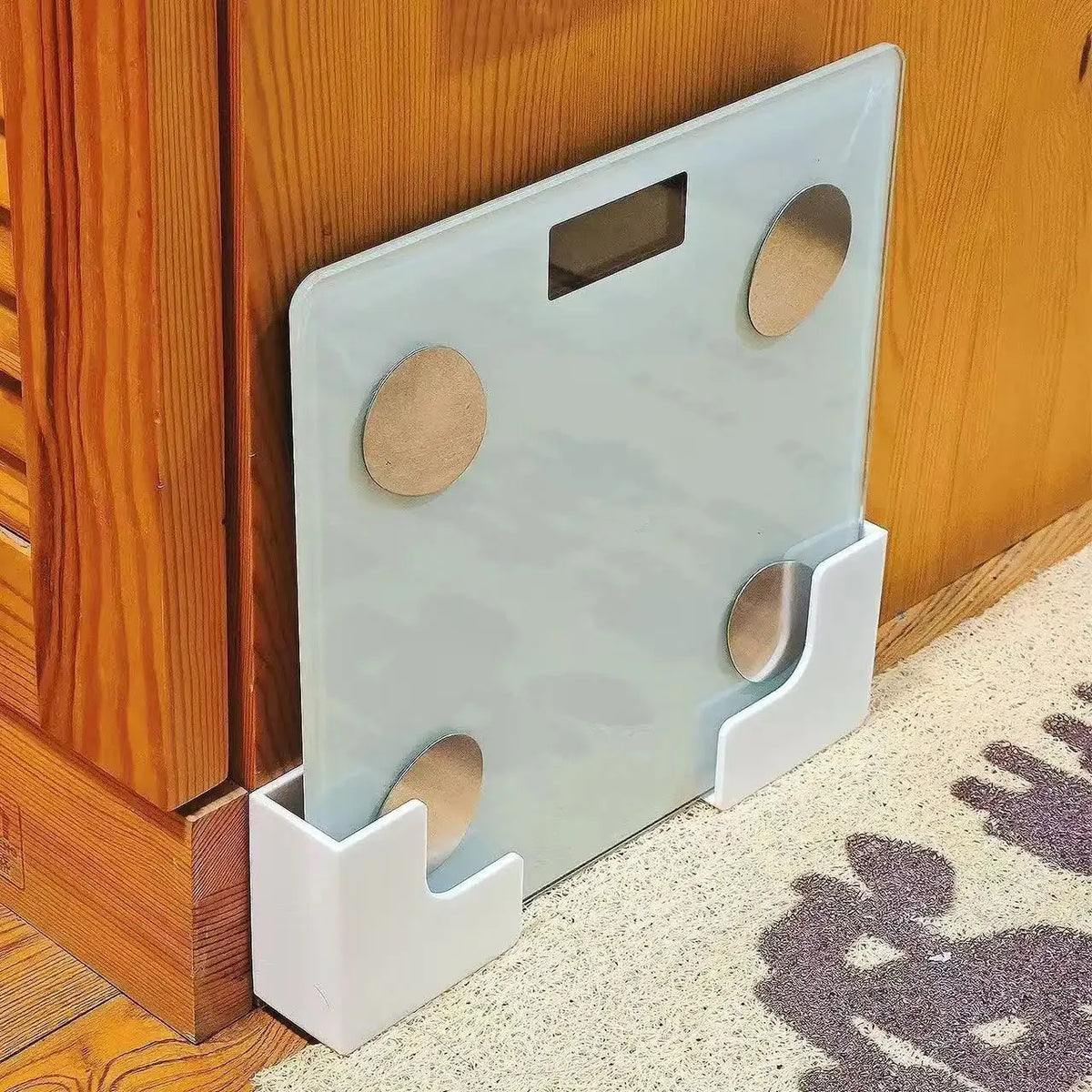 A light blue wall-mounted storage holder for a scale with self-adhesive mounting features.