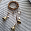 A vintage wicker wreath with hanging brass bells and beads displayed on a gray textured surface.