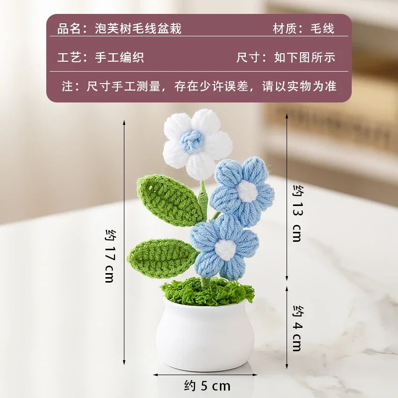 A cluster of hand-woven crochet flowers in blue and white are displayed in a white pot on a marble surface.