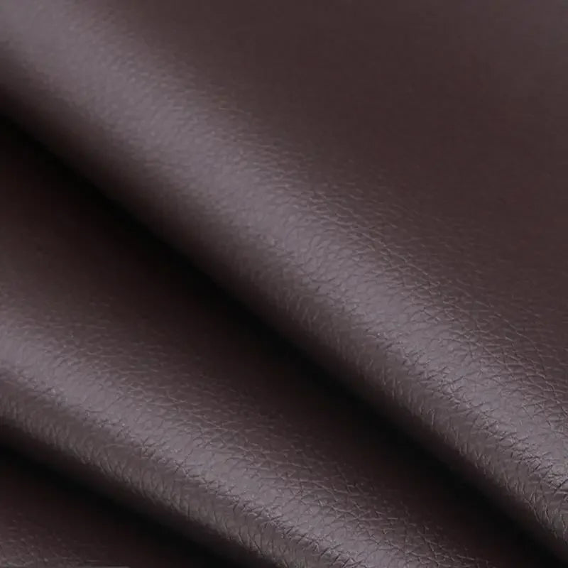 Close-up of a dark brown self-adhesive PU leather repair patch being applied to a material.