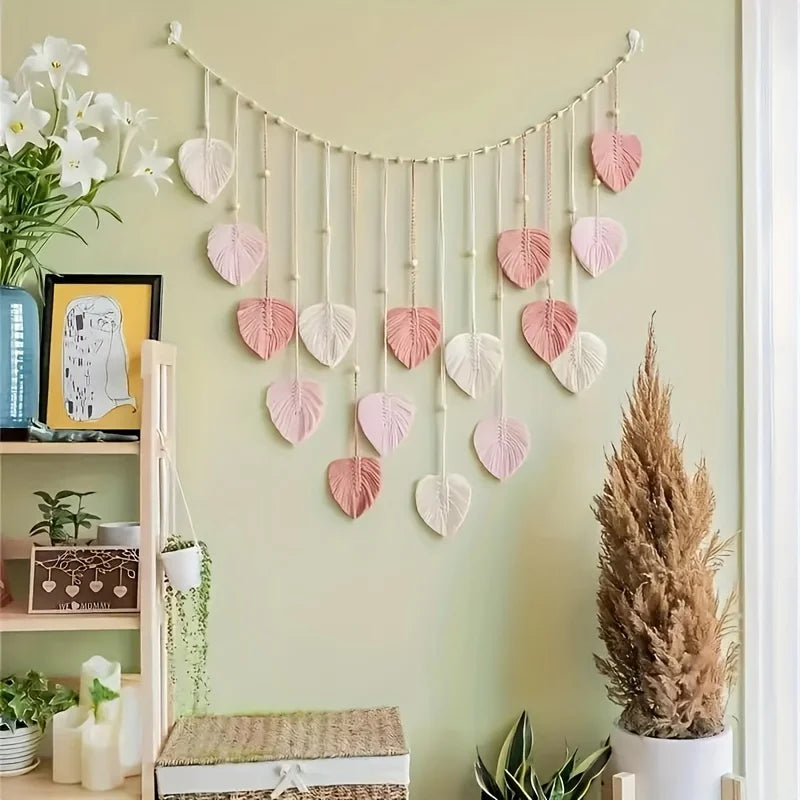 Handwoven pink leaf tassel wall hanging displayed on a light green wall.