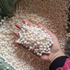 A hand holds a pile of small white foam beads scattered on a textured orange background.