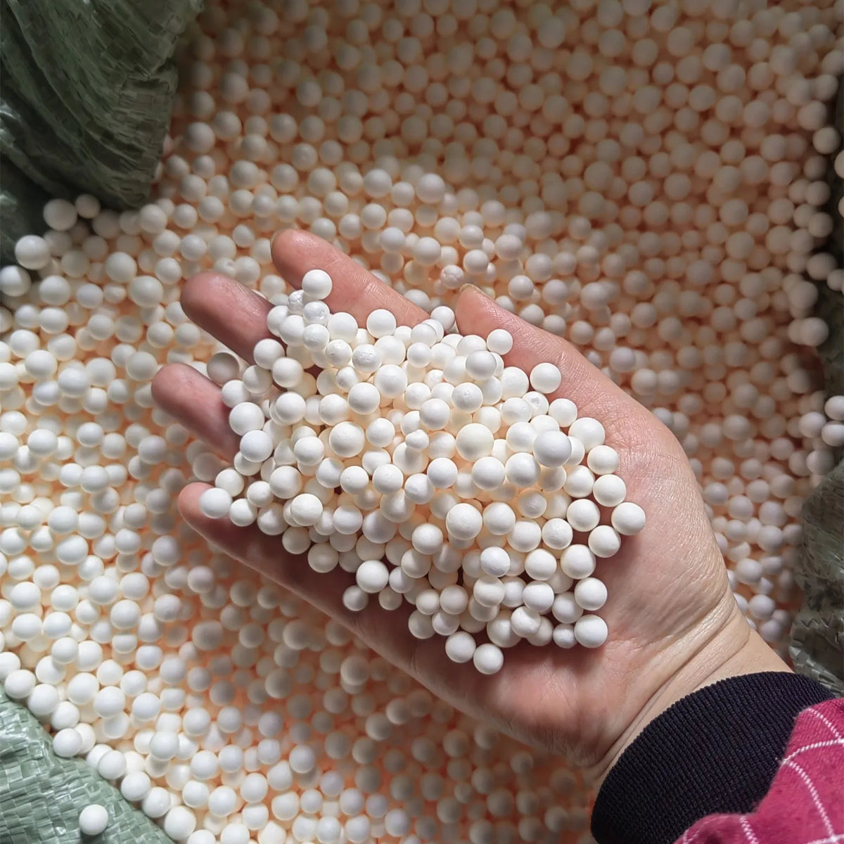 A hand holds a pile of small white foam beads scattered on a textured orange background.