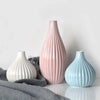 A pink ceramic flower vase with vertical ridges sits on a white surface next to a light blue one.
