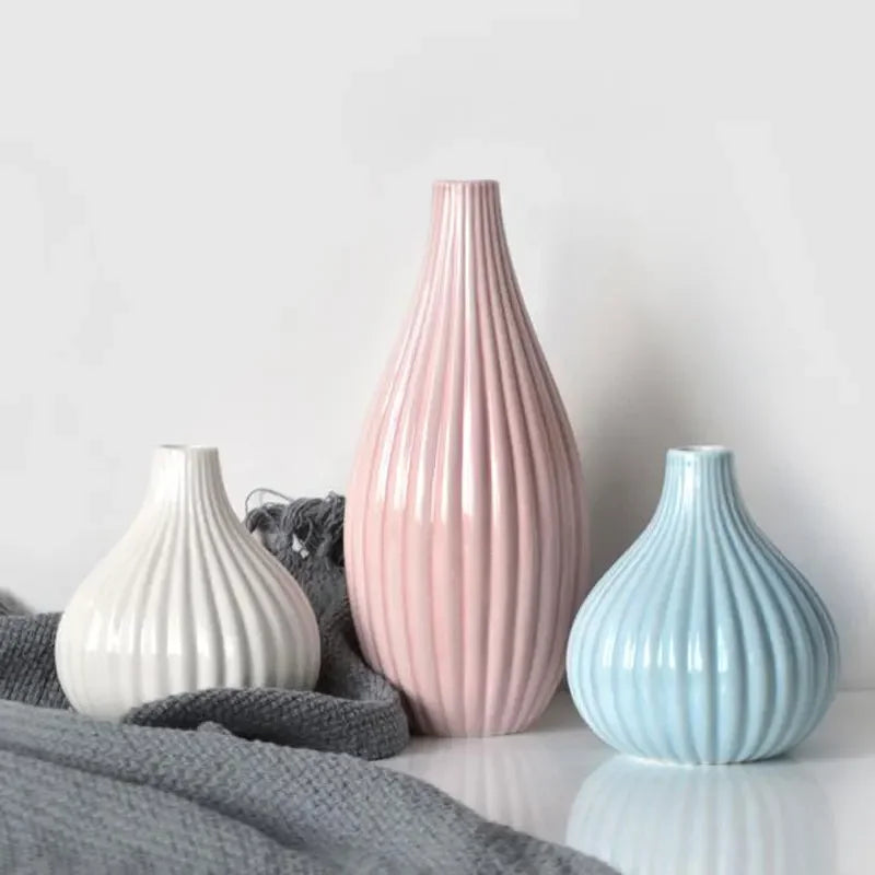 A pink ceramic flower vase with vertical ridges sits on a white surface next to a light blue one.