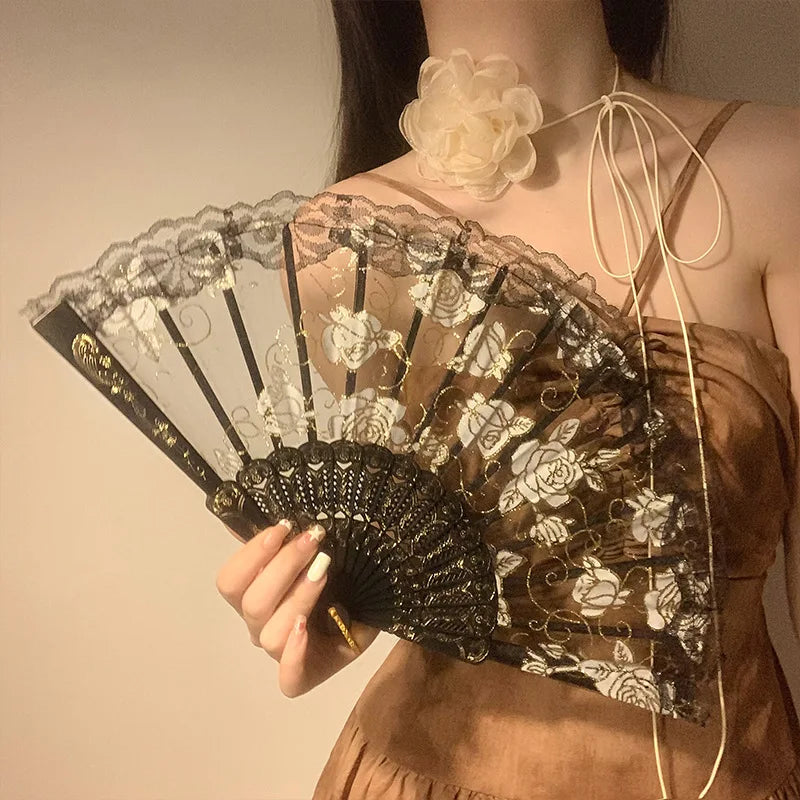 A close-up of an elegant black and white lace rose folding fan being held against a woman's chest.