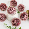 A collection of dried silk peony artificial flowers in dusty rose and mauve shades arranged on a white surface.