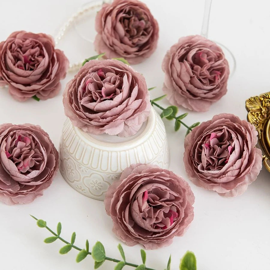 A collection of dried silk peony artificial flowers in dusty rose and mauve shades arranged on a white surface.