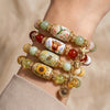A stack of nature-inspired stretch charm bracelets featuring green and amber beads and floral charms on a wrist.