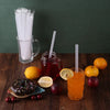 A glass jar filled with red juice sits next to various citrus fruits and dark treats on a wooden surface.