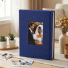 A dark blue linen photo album with a square window displaying a portrait of a bride and groom.