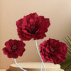 A cluster of deep red velvet artificial peony flowers on white stems against a beige background.