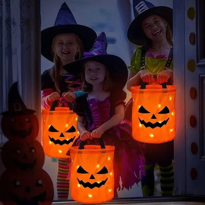 Three children wearing witch hats hold orange pumpkin tote bags with LED light-up handles.