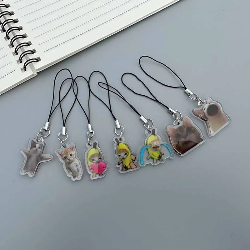 A collection of acrylic keychains featuring cute animal figures like cats and a banana, hanging from black cord.