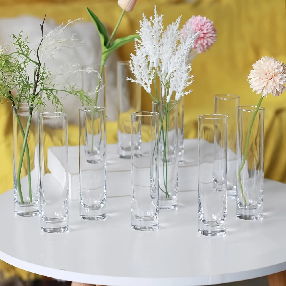 A set of twelve clear glass cylinder vases with floral arrangements displayed on a white table.