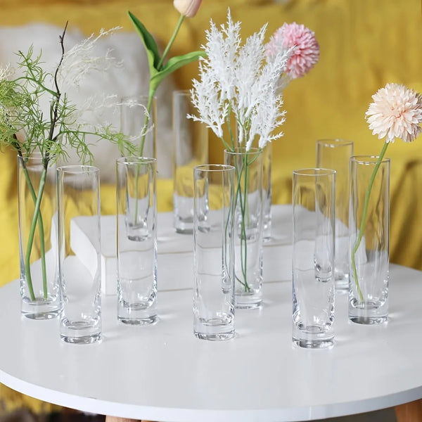 A set of twelve clear glass cylinder vases with floral arrangements displayed on a white table.