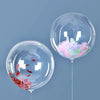 Two clear balloons filled with pink and green confetti float against a solid blue-gray background.