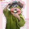 A person wearing a fuzzy green monster onesie pajama with large pink lips and an electronic device.