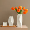 A modern white plastic decorative vase holds a bouquet of vibrant orange tulips against a neutral background.