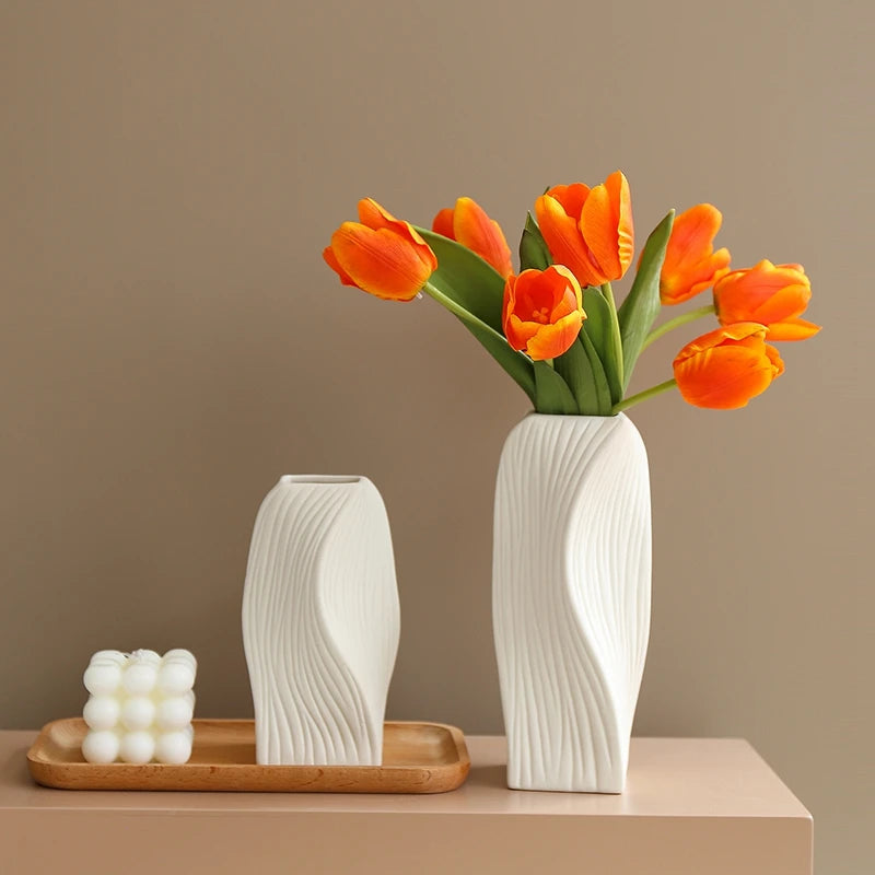 A modern white plastic decorative vase holds a bouquet of vibrant orange tulips against a neutral background.