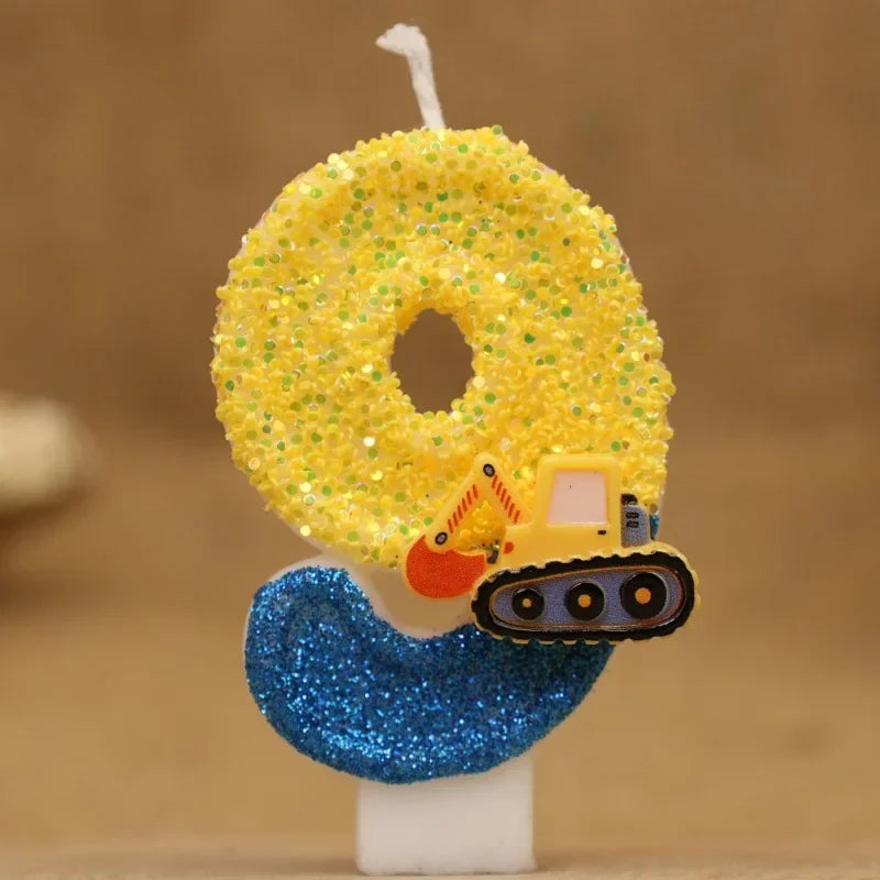 A yellow construction excavator shaped candle decorated with gold glitter and a blue glitter base.