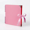 Bloc-notes d'album rose à plat avec une reliure rouge et un ruban rose attaché à la couverture.