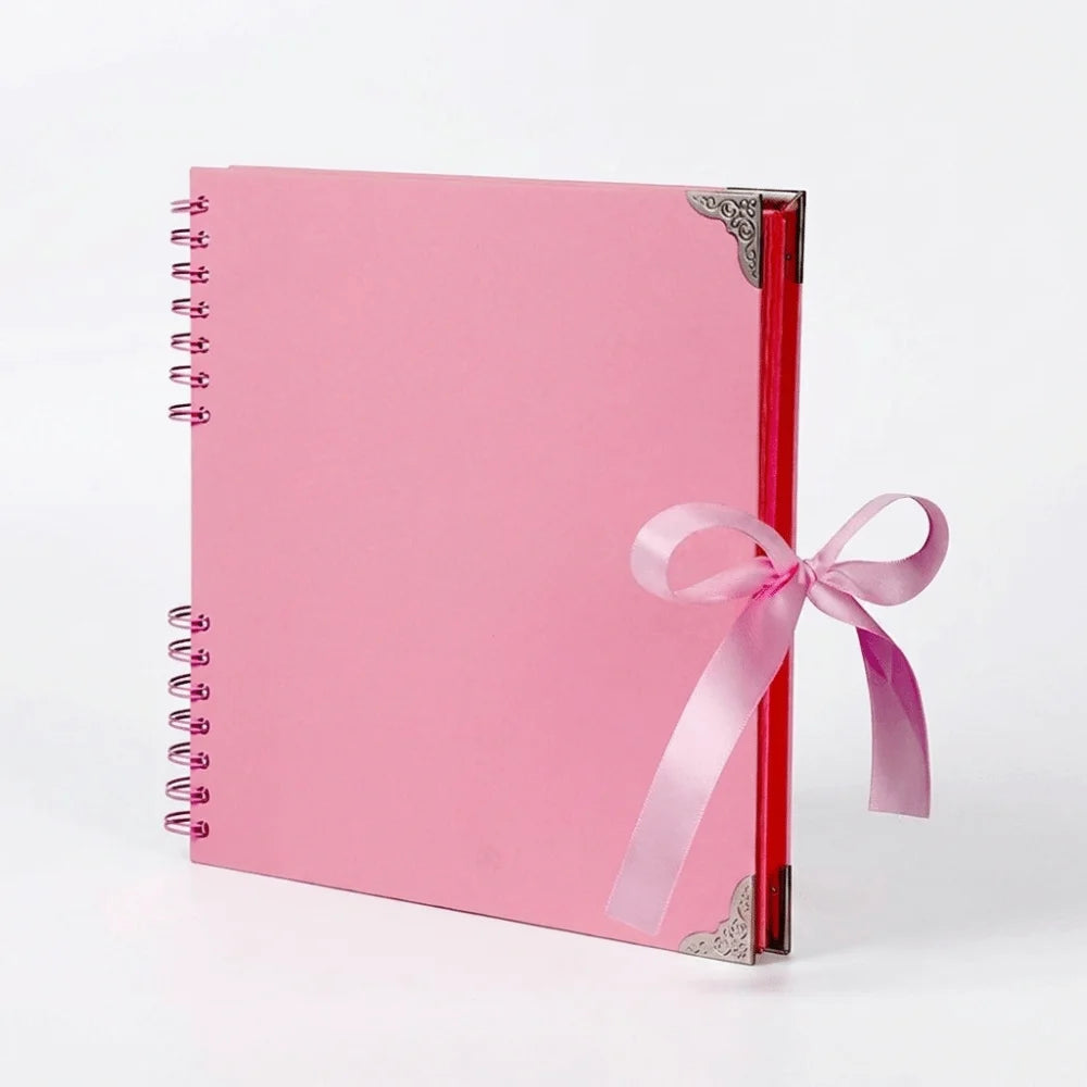 Bloc-notes d'album rose à plat avec une reliure rouge et un ruban rose attaché à la couverture.