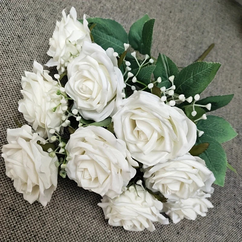 A bouquet of white silk peonies with green leaves and small white filler flowers.