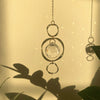 Une délicate chaîne en or avec un pendentif de cristal clair, projetant des ombres sur un fond clair.