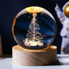 A crystal ball decoration featuring a laser engraved silhouette of a Christmas tree and stars against a dark blue background.