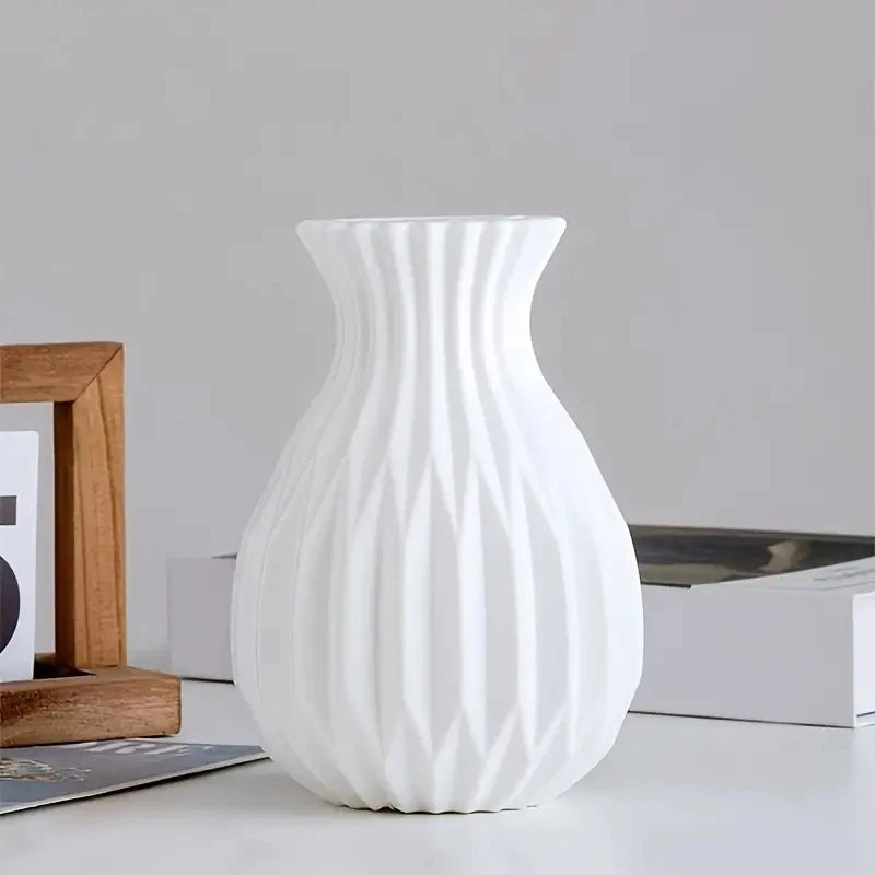 A white ceramic flower vase with vertical ribbed texture sits on a white surface.