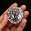 A clear coin featuring a depiction of Saint Michael the Archangel surrounded by wings and ornate design.