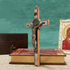 A silver crucifix featuring a figure of Christ, St. Benedict medal, and INRI, displayed on a wooden book.