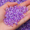 A hand holds a pile of small, round purple AB crystal glass beads for jewelry making.