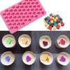 A pink silicone mold tray with hemispherical cavities and a colorful assortment of silicone candy molds.